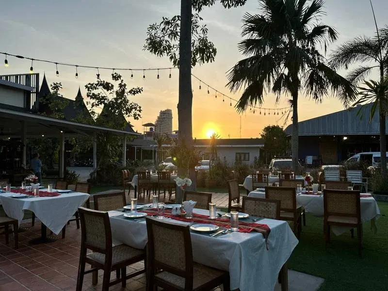 Garden tables set for dinner at sunset, under string lights and palm trees