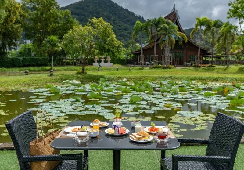 A table set beside the lotus pond, with Thai-style pavilions and green hills behind